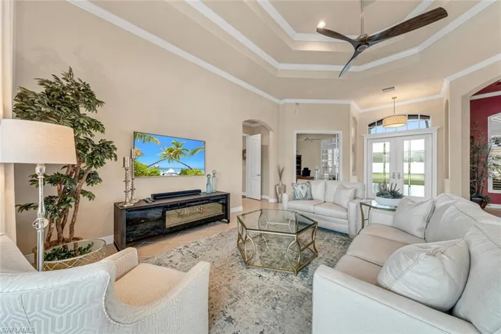 Tiled living room featuring a tray ceiling, french doors, crown molding, and ceiling fan