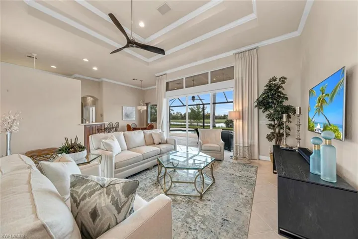 Living room featuring a tray ceiling, ceiling fan, ornamental molding, and light tile patterned floors