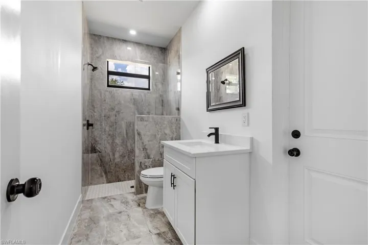 Bathroom with vanity, tiled shower, toilet, and tile patterned flooring