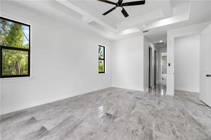 Tiled empty room featuring ceiling fan, a raised ceiling, and a healthy amount of sunlight