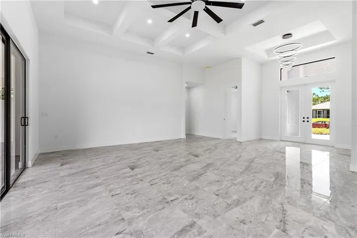 Spare room featuring beamed ceiling, coffered ceiling, light tile patterned floors, and ceiling fan