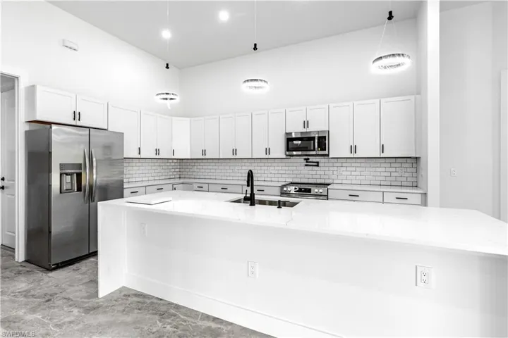 Kitchen with pendant lighting, light stone countertops, a center island with sink, and stainless steel appliances