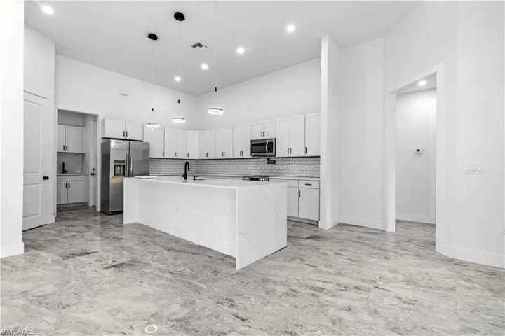 Kitchen featuring stainless steel appliances, decorative light fixtures, light tile patterned floors, decorative backsplash, and an island with sink