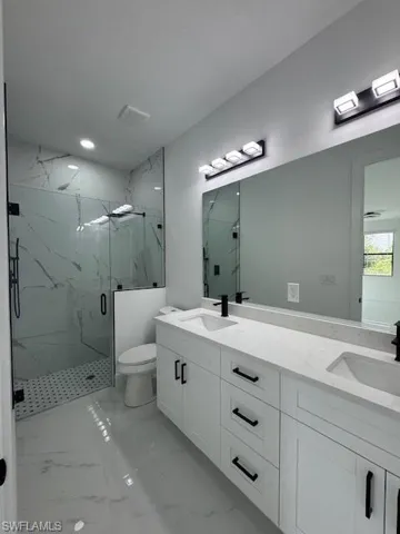 Bathroom featuring a marble finish shower, double vanity, light marble finish floors, and recessed lighting