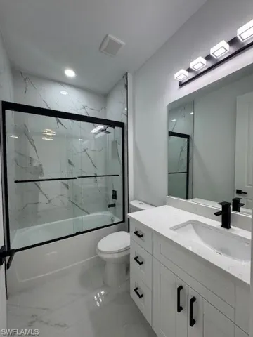 Bathroom featuring enclosed tub / shower combo, vanity, and light marble finish floors
