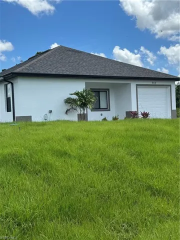 Front of house with stucco siding, an attached garage, a shingled roof, and a lawn