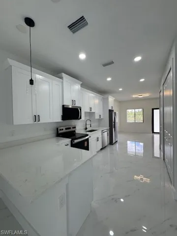 Kitchen with a peninsula, white cabinetry, light marble finish flooring, stainless steel appliances, and light stone counters