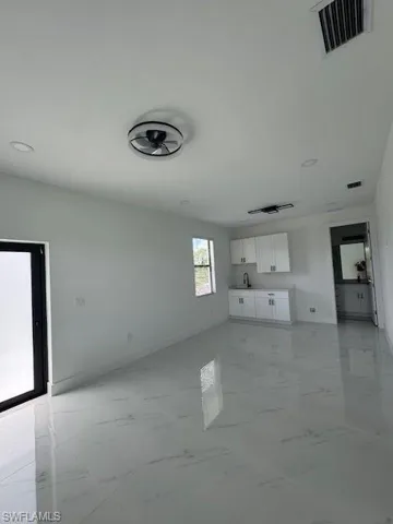 Unfurnished living room featuring light marble finish flooring and baseboards