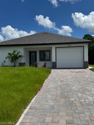 Single story home featuring a garage, decorative driveway, stucco siding, and a shingled roof