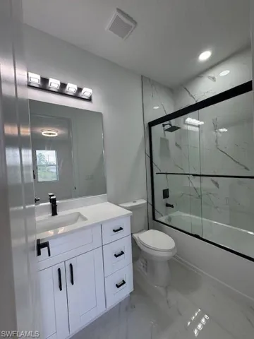 Bathroom featuring vanity, shower / bath combination with glass door, and light marble finish floors