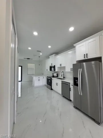 Kitchen with a peninsula, stainless steel appliances, white cabinetry, light marble finish floors, and recessed lighting