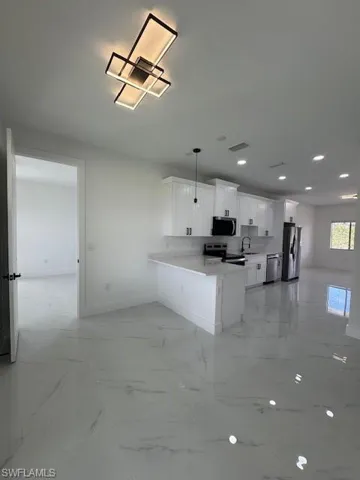 Kitchen featuring white cabinetry, decorative light fixtures, a peninsula, range, and light marble finish flooring