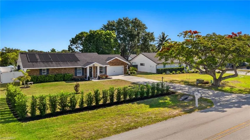 Single story home featuring a garage, solar panels, and a front lawn