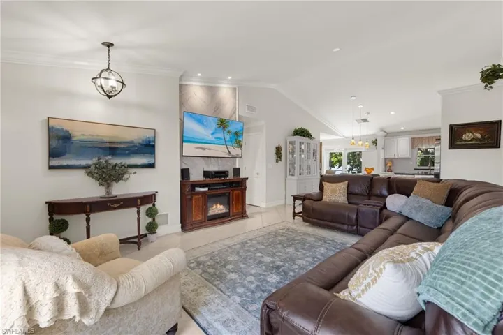 Living room featuring ornamental molding, lofted ceiling, a fireplace, a chandelier, and light tile flooring