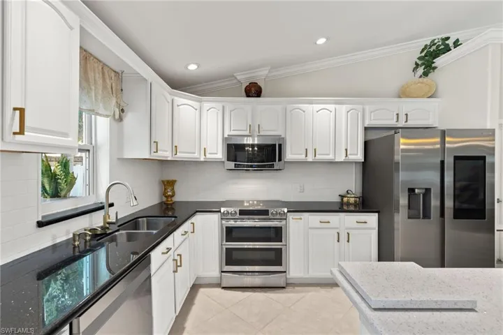 Kitchen featuring ornamental molding, appliances with stainless steel finishes, white cabinets, vaulted ceiling, and light tile floors