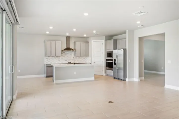 Kitchen with appliances with stainless steel finishes, gray cabinets, wall chimney range hood, decorative backsplash, and recessed lighting