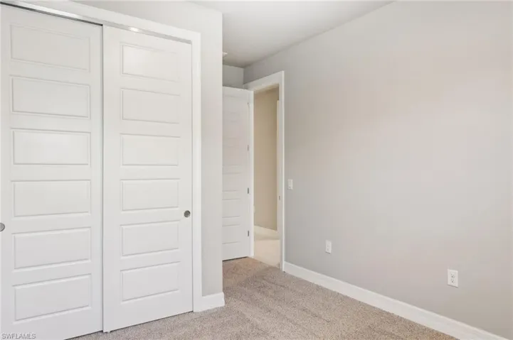 Unfurnished bedroom with light colored carpet, a closet, and baseboards
