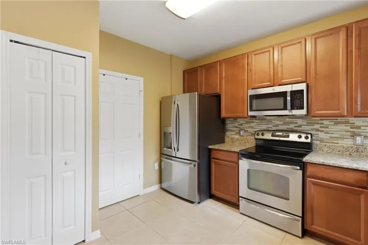 Functional kitchen featuring stainless steel appliances, light wood-finish cabinetry, granite-style countertops, and a mosaic tile backsplash