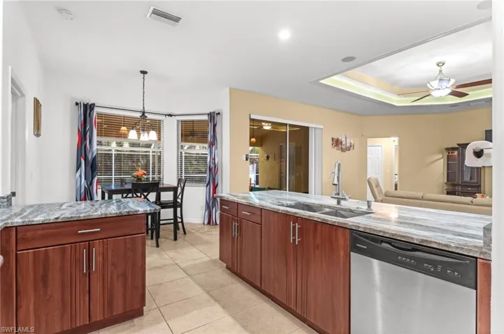 Kitchen with stone countertops, wood-finish cabinetry, stainless steel dishwasher, and tile flooring