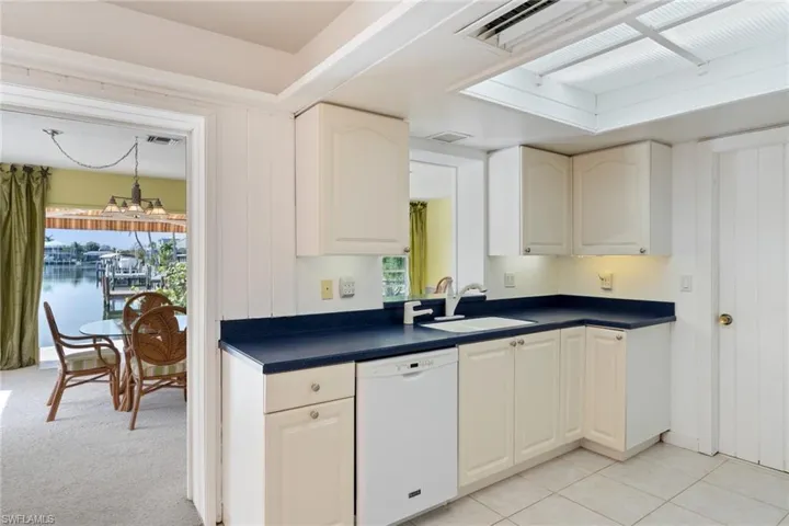Kitchen featuring white dishwasher, dark countertops, a chandelier, and plenty of natural light