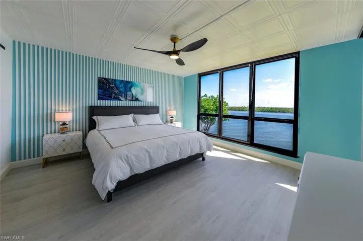 OWNER'S SUITE HAS FLOOR-TO-CEILING ESTERO BAY VIEWS.  IMPACT GLASS WINDOWS.  ENTRANCE TO LANAI IS TO RIGHT.  BED FRAME W/LED ACCENT LIGHTS.  LUXURY VINYL PLANK TILE FLOORING.  FLUTED WOOD ACCENT WALL.  CUSTOM ZEBRA BLINDS.  ENTRANCE TO EN-SUITE BATH IS TO LEFT.