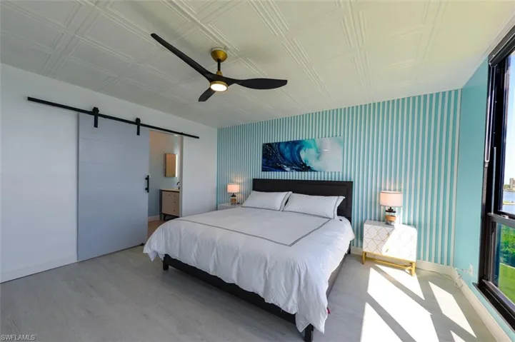 OWNER'S SUITE.  TRACK BARN DOOR ENTRANCE TO EN-SUITE BATH AND WALK-IN CLOSET.  PVC CEILING TILE.  FLUTED WOOD ACCENT WALL.  LUXURY VINYL PLANK TILE FLOORING.
