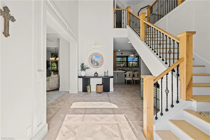 Grand entry foyer featuring light wood-finish flooring with a geometric pattern, a prominent staircase with wood handrails and wrought iron balusters, and high ceilings