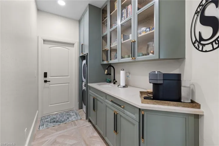 Dedicated utility space featuring stacked laundry appliances, light green cabinetry with gold-tone hardware, and a single-basin sink with a matte black faucet