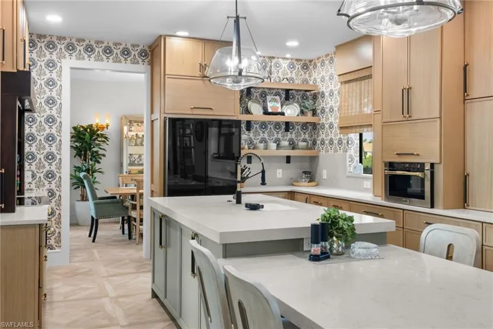 Gourmet kitchen featuring a central island with integrated seating, light wood-finish cabinetry, built-in stainless steel appliances, and decorative accent wallpaper
