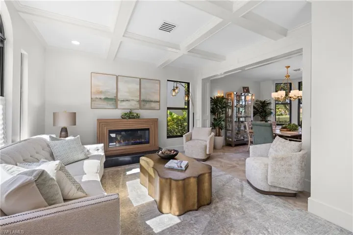 Living area featuring a coffered ceiling, a contemporary fireplace with a wood surround, and light-tone flooring