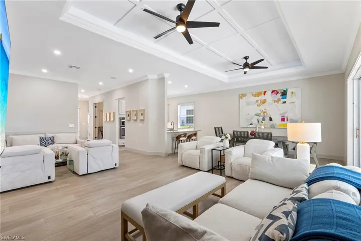 The open concept living area features light-toned flooring, recessed lighting, and a coffered ceiling with ceiling fans