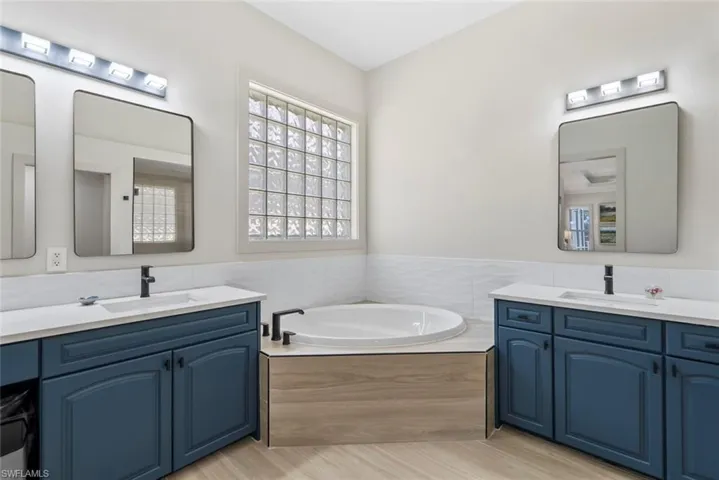 Bathroom featuring a soaking tub, two separate vanities with sinks, and a large privacy window with glass blocks