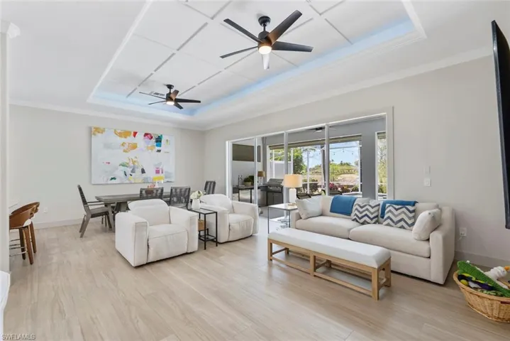The property features an open living space with light-toned flooring, a decorative tray ceiling with two ceiling fans, and sliding glass doors that open to an outdoor area