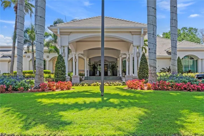 The property features a grand entrance with a covered portico, surrounded by a well-maintained lawn and vibrant landscaping