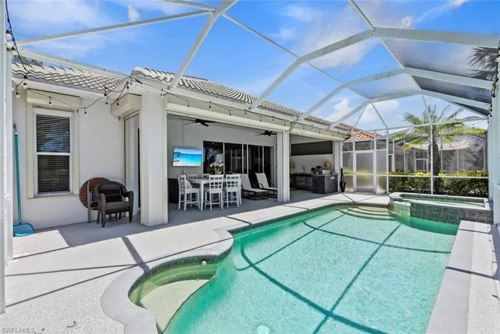 Screened-in outdoor living area featuring a swimming pool, an integrated spa, and a covered patio with an outdoor kitchen