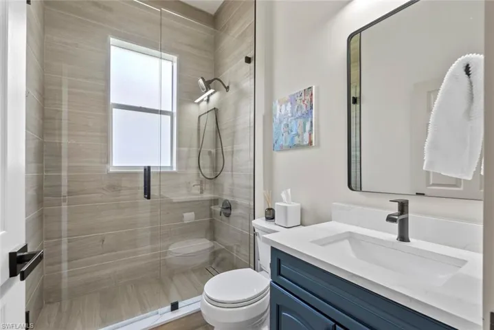 Bathroom featuring a glass-enclosed shower with tiled walls, a vanity with a white countertop and dark blue cabinetry, and a rectangular mirror with a dark frame