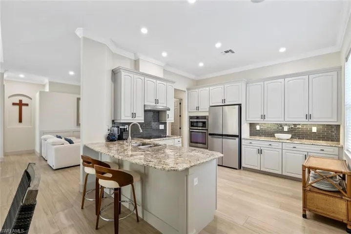 The kitchen features light-toned cabinetry, stainless steel appliances, a large island with a granite countertop, and a tiled backsplash