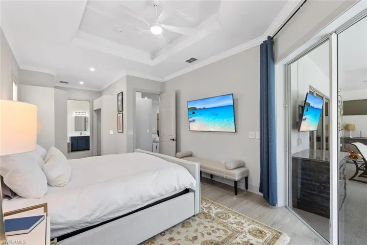 Bedroom with tray ceilings, a ceiling fan, and light-toned flooring, featuring a large bed and direct access to an outdoor area through sliding glass doors