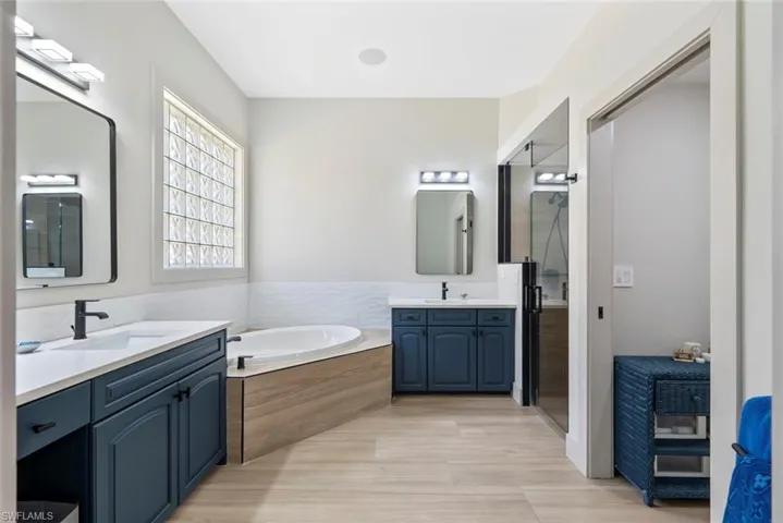 The bathroom features a built-in tub with a wood-paneled surround, two separate vanities with dark blue cabinetry, and light-colored flooring