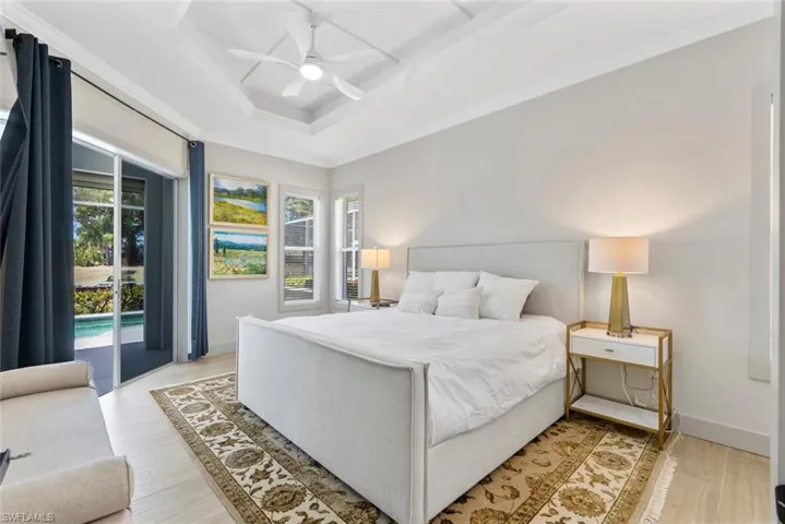 This room features a tray ceiling with a ceiling fan, light wood flooring, and direct access to a patio with a visible pool