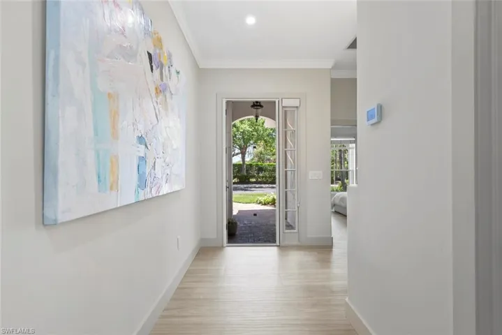 Entryway featuring light-toned flooring, white crown molding, and an arched door leading to an outdoor area with greenery