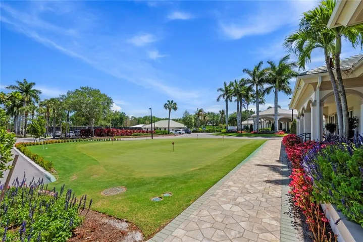 The property features a well-maintained putting green, a paved walkway, and manicured landscaping with vibrant flowering shrubs