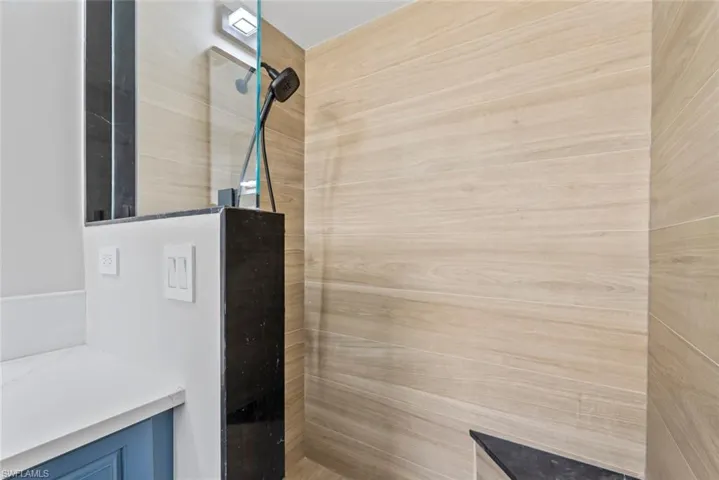 The shower features light-toned tiled walls, a dark-toned showerhead, and a glass partition