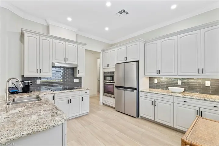 Well-appointed kitchen featuring light-toned cabinetry, granite countertops, stainless steel appliances, and a tiled backsplash