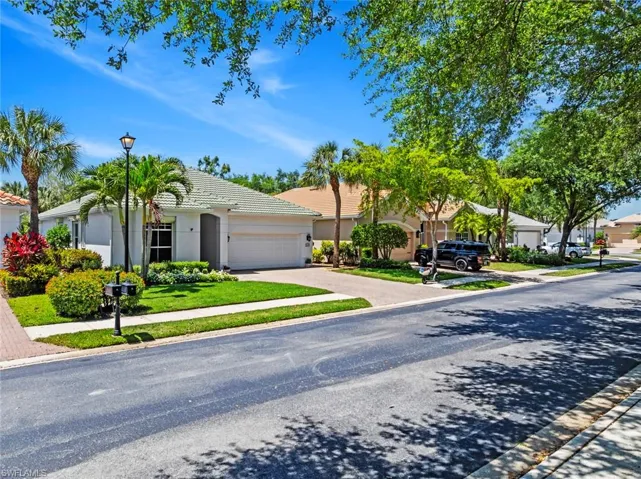The property features a well-maintained lawn, mature landscaping with palm trees and shrubs, and a paved driveway leading to a two-car garage