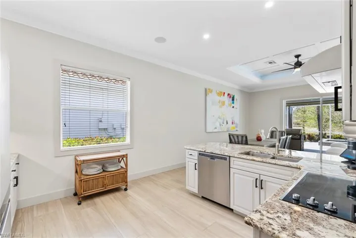 The open concept living area features tray ceilings with recessed lighting and ceiling fans, light wood-look flooring, and a kitchen with white cabinetry, stainless steel appliances, and a tiled backsplash