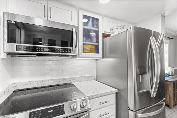 Kitchen featuring stainless steel appliances, white cabinets, light stone countertops, and tasteful backsplash