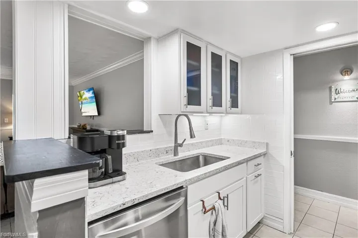 Kitchen with dishwasher, light stone counters, white cabinets, glass insert cabinets, and light tile patterned floors