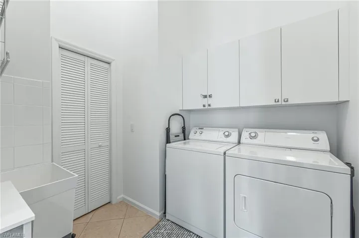 Laundry area with light tile patterned flooring, washing machine and dryer, and cabinet space