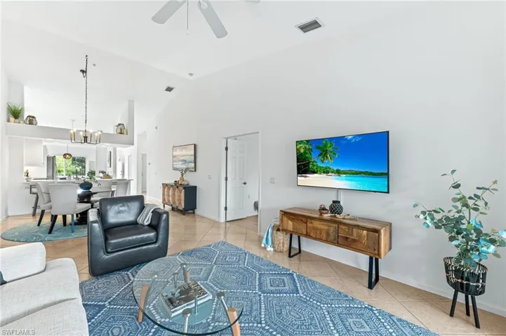 Living area with light tile patterned flooring, high vaulted ceiling, a chandelier, and ceiling fan